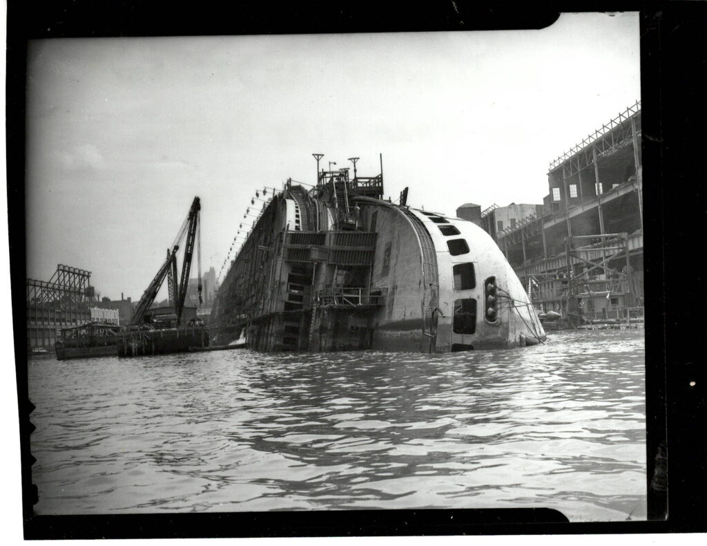 Docked at the 48th pier, on February 9, 1942, the French ocean liner Normandie (renamed the USS Lafayette) caught fire and capsized on its side. Courtesy Cipollini Collection